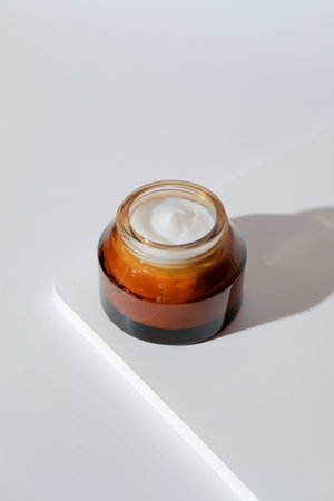 Amber glass jar with natural moisturizer face cream on white podium. Organic beauty product...