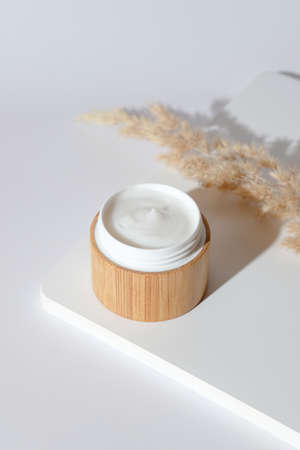 Natural face cream in eco friendly bamboo jar on white podium. Organic skin care cosmetics. Beauty product packaging design.の写真素材
