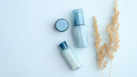 Flat lay blue transparent cosmetic bottles, cream jar and dry flowers on blue background. Top view SPA natural organic beauty products. Skin care concept.の写真素材