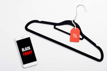 Black Friday Sale concept. Smartphone with sign "Black Friday" on screen and clothes hanger on white table.の写真素材