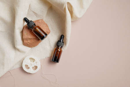 Essential oil bottles and loofah on brown background with beige fabric. Body treatment concept. Flat lay, top view.の写真素材