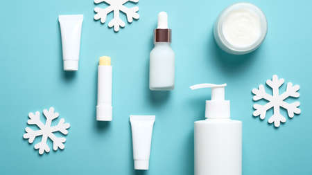 Skincare cosmetic, winter treatment, packaging design template. Dropper bottle with serum, lipstick, pump bottle, jar of moisturizer cream, tubes and snowflakes on blue background. Flat lay, top view.の写真素材