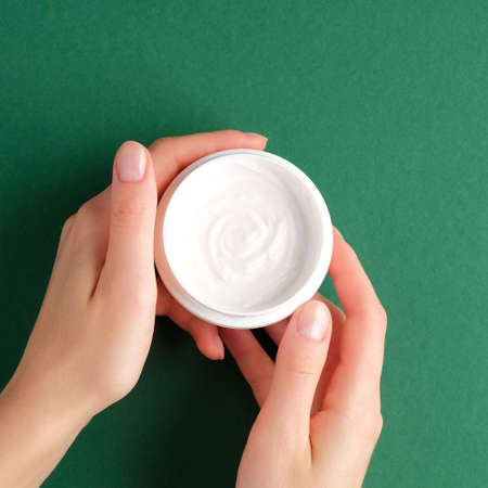 Female hands holding jar of moisturizer cosmetic cream over green background. SPA natural organic beauty product.の写真素材
