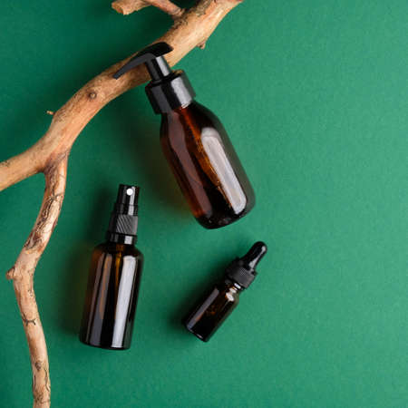 Amber glass packages with natural cosmetics and wooden branch on green background. Flat lay, top view. Bio organic product. Beauty and spa concept.の写真素材