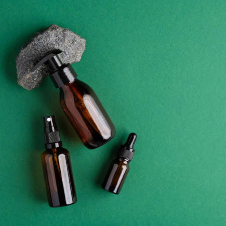 Amber glass cosmetic bottles and stone on green background. Flat lay, top view. Bio nature cosmetics skin care conceptの写真素材