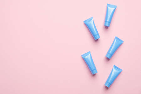 Many blue cosmetics tube packaging on pink background. Top view with copy space. Skin care, beauty treatment concept.の写真素材