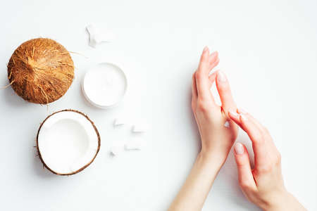 Female hands applying coconut cream on white background. Coconut organic cosmetics, oil, lotion for hand skin care, natural moisturizer, health and beauty concept. Flat lay, top viewの写真素材