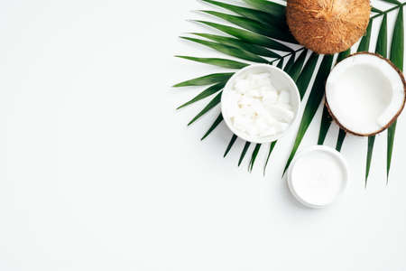 Flat lay composition with coconut oil body cream, coconut half, grated coconut in bowl and tropical palm leaf on white background. SPA natural organic cosmetic, body care conceptの写真素材