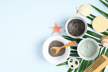 Face clay masks in bowls with tropical palm leaf on blue background, top view. Facial skincare, SPA...