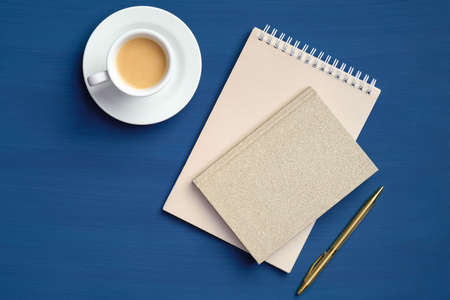 Cup of coffee with blank paper notebook and notepad on dark blue table. Flat lay, top view. Office coffee break conceptの写真素材