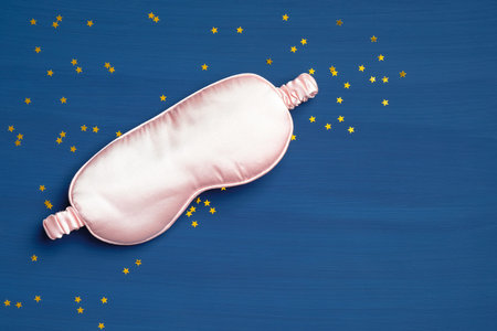 Pink blindfold on classic blue background with confetti. Sleep mask for eyes, relaxation and protection. Flat lay, top viewの写真素材