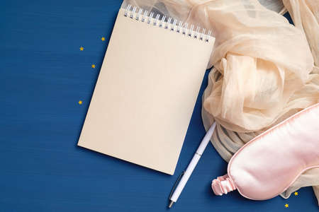 Sleep journal with eye mask and blanket on dark blue background. Writing dreams, fall asleep, insomnia concept. Flat lay, top viewの写真素材