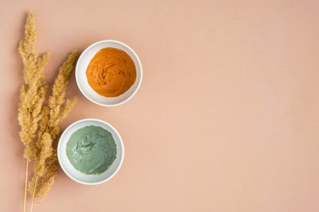 Healing clay masks and dry flowers on peach background. Natural organic SPA cosmetic products, facial skin treatment concept. Flat lay, top view.の写真素材