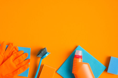 House cleaning supplies on orange background. Top view blue sponge, brush, napkin with cleaner...