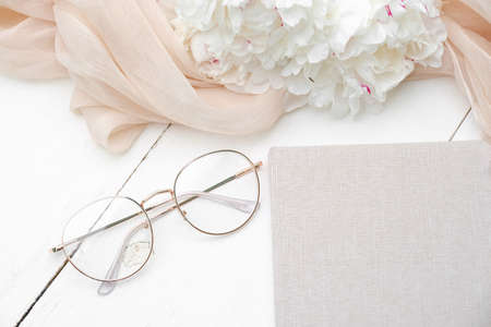 Female workspace with paper notebook, glasses, beige cloth on white wooden background. Flat lay, top view. Beauty blogger workplaceの写真素材