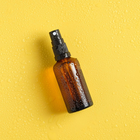 Summer sunscreen lotion bottle in droplets of water on yellow background. Flat lay, top view. Summer sun protection concept.の写真素材