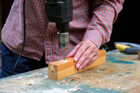 Close-up of female carpenter drilling wooden plank to make hole. DIY, woodwork concept.