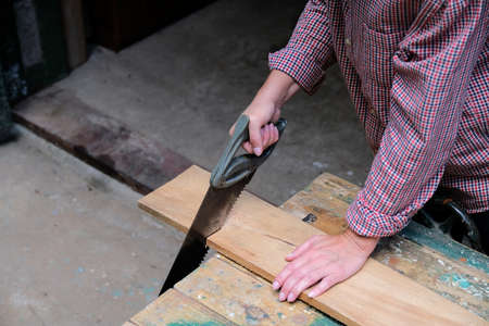 Carpenter woman cutting a board with a hand saw. Carpentry, construction, woodworking concept.の写真素材