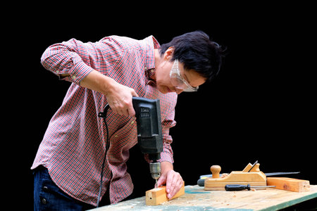 50 years old woman carpenter drilling a hole with an electric drill machine in wooden plank....