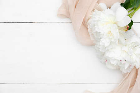 Flat lay composition with peonies and beige cloth on white wooden table. Greeting card mockup for Mother's Day, Woman's Day, wedding celebration. Top view with copy spaceの写真素材
