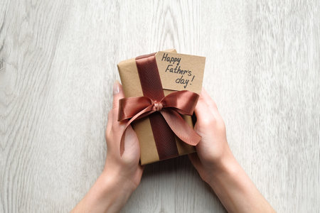 Womans hands holding gift box wrapped festive ribbon and label with text Happy Father's Day on...
