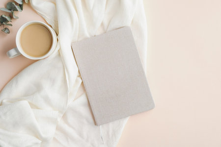 Flat lay, top view home office desk table with paper notebook, blanket and cup of coffee on beige background. Modern feminine workspace concept.の写真素材
