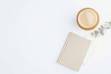Flat lay, top view office table desk. Feminine workspace with eucalyptus leaves, paper notebook, envelope and coffee cup on white background. Business concept.の写真素材