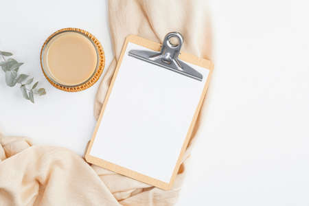 Modern home office desk with clipboard mockup, cup of coffee, beige blanket and eucalyptus flower on white background. Freelancer workspace concept. Flat lay, top view.の写真素材