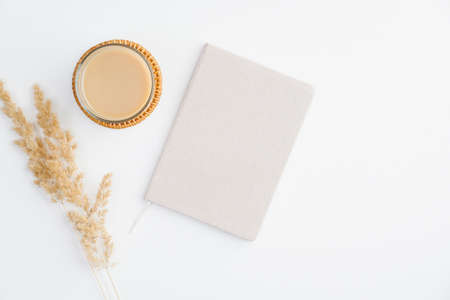 Simple trendy office desk with notebook, cup of coffee and dry reeds on white background. Minimal style feminine workspace.の写真素材