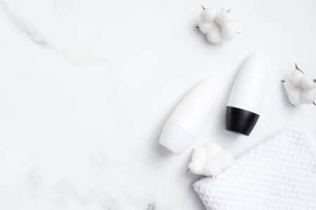 Roll-on deodorant with cotton flowers and towel on marble background. Antiperspirant packaging mockup, sweat protection concept. Flat lay, top viewの写真素材
