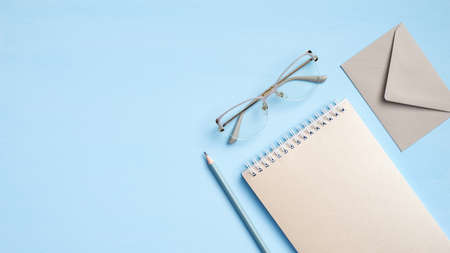 Stylish feminine workspace with paper notebook, glasses, envelope, pen on blue background. Modern office desk table, flat lay, top view. Business conceptの写真素材
