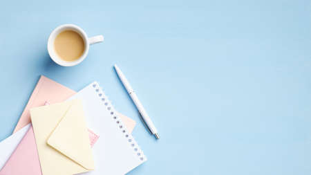Modern office desk table with cup of coffee and heap of paper notebook, notepad, stationery on blue background. Flat lay, top view, copy space. Business or education conceptの写真素材
