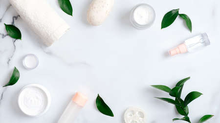 Natural cosmetic products and green leaves on marble background. Frame made of towel, handmade soap, essential oil, luffa sponge, hand cream. Flat lay, top view. Natural organic beauty product conceptの写真素材