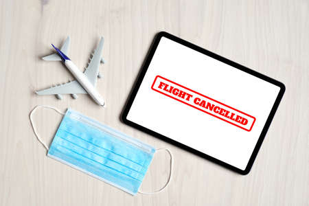 Coronavirus flight cancellations concept. Top view airplane toy, digital tablet with message "Flight canceled" on screen and face mask.の写真素材
