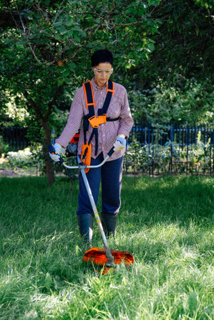 Woman worker mowing the grass in garden using string trimmer