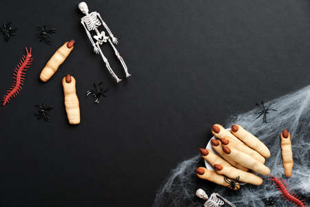 Halloween finger cookies, spiderweb, skeletons on black background. Halloween holiday celebration concept. Flat lay, top view, overhead.の写真素材