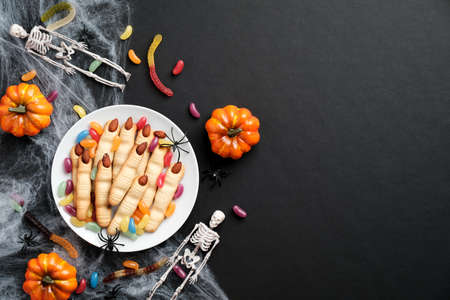 Happy Halloween holiday concept. Halloween cookies in form of witches fingers, pumpkins, skeletons, spiderweb, festive decorations on black background. Flat lay, top view.の写真素材
