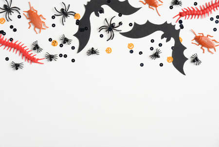 Happy halloween holiday concept. Frame border made of halloween decorations, bats, spiders, insects, confetti on white background. Halloween party greeting card mockup. Top view, copy space.の写真素材