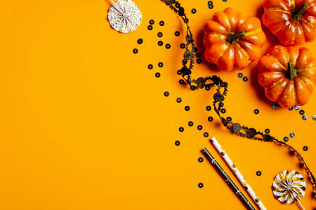 Happy halloween holiday concept. Halloween party decorations, confetti, pumpkins, black ribbon on orange background. Halloween party invitation card mockup with copy space. Flat lay, top viewの写真素材