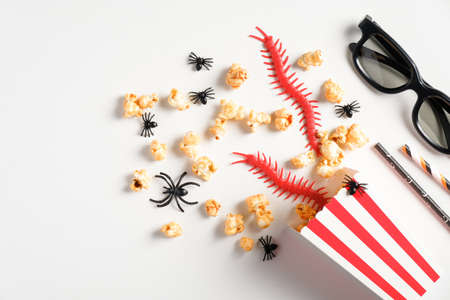 Halloween party background. Flat lay composition with popcorn, halloween decorations, 3d glasses on white table. Watching halloween horror movie at night concept.の写真素材