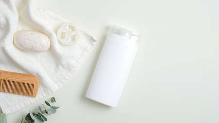 Hair care product design concept. SPA cosmetic bottle packaging, wooden hair comb, white towel, organic soap, luffa sponge on green background. Minimalist cosmetic product mockup, natural brandingの写真素材