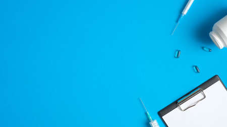 Frame border of medical tools and equipment on blue background. Top view doctor table with syringes, medical clipboard and pills. Medical banner design, header template. Healthcare and medical conceptの写真素材