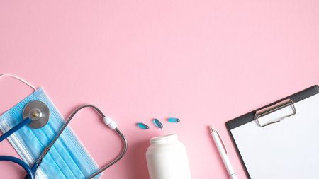 Medical equipment on pink background. Flat lay surgical mask, stethoscope, pills, medical clipboard...