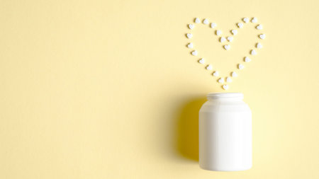 White medical bottle and cardiac medications in heart shape spilling out on to pastel yellow...