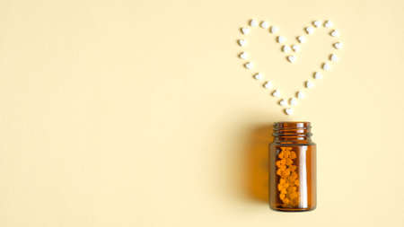 Heart shape from pills pilling from a glass bottle. Pharmacy store, medical clinic, drugstore banner design template. Medical tablets, drug of painkillers, antibiotics, vitamins. Flat lay, top viewの写真素材