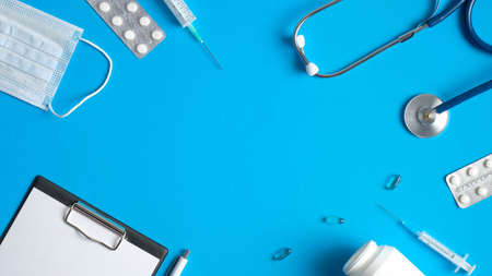 Frame of medical equipment, tools, supplies on blue background. Top view doctor table with medical clipboard, stethoscope, syringes, pills. Medical banner design. Healthcare and medicine concept.の写真素材