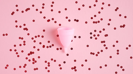 Reusable menstrual cup on pink background with confetti. Alternative menstrual hygiene product....