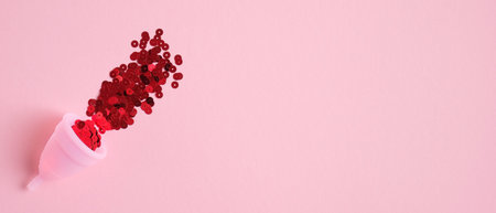 Menstrual cup filled red confetti on pink background with copy space. Banner design for beauty blog....