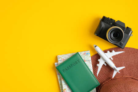 Top view of traveler accessories. Flat lay beach hat, passport, map, airplane, photo camera on yellow background with copy space. Travel summer holiday vacation banner conceptの写真素材