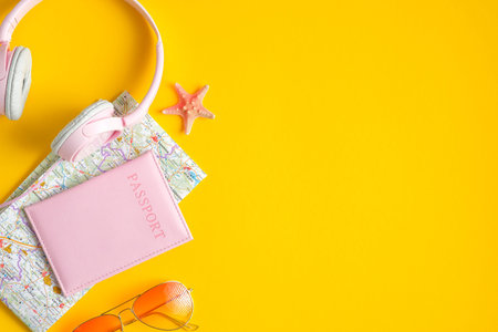 Stylish traveler accessories on yellow background. Flat lay pink headphones, passport, map,...